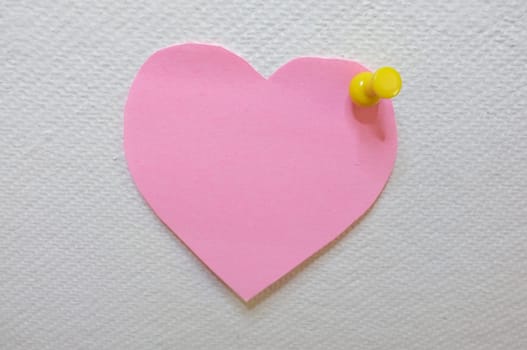 Note paper in heart shape with yellow pin posted on white cork board background
