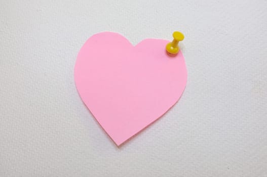 Note paper in heart shape with yellow pin posted on white cork board background