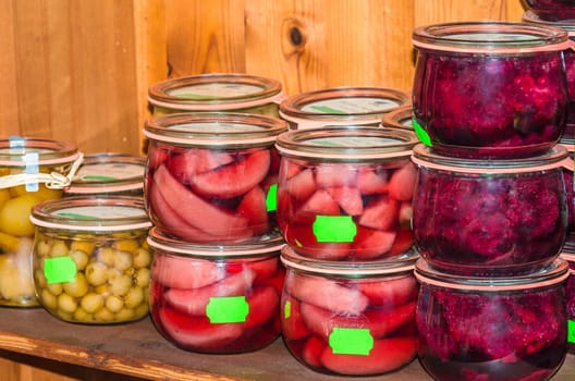 Wooden shelf filled with mason jars with different types of fruits.