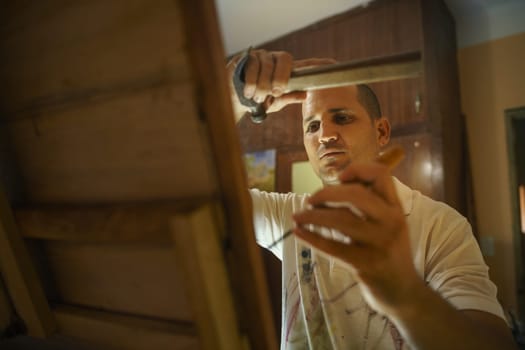 Adult man at work as artist, chiselling a bas-relief in his atelier. He works with hammer and ceasel on a wood painting.