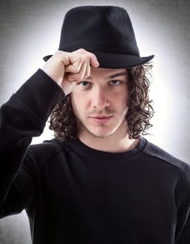 Portrait of young man dressed in black greet someone with hat