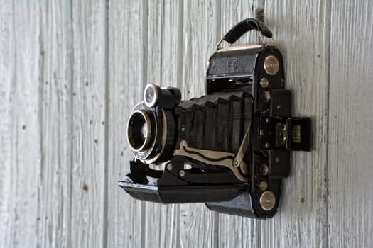Black old camera hangs on old,white painted wooden wall