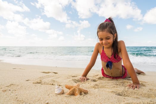 smiling little girl plays with a starfish on the beach on a summer day