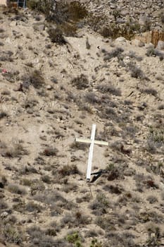 A wooden cross stands on a hill in the middle of a barren desert landscape.
