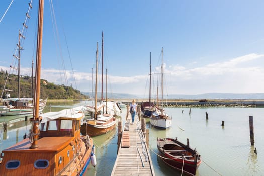 Woman strolls along wooden pier between traditional fishing boats at old fishing port in Secovlje, Slovenia. Summertime feeling. Landscape format.