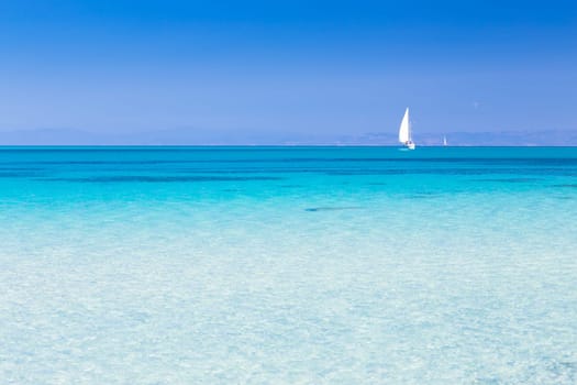 White sail boat at the beautiful turquoise blue mediterranean Pelosa beach near Stintino,Sardinia, Italy.