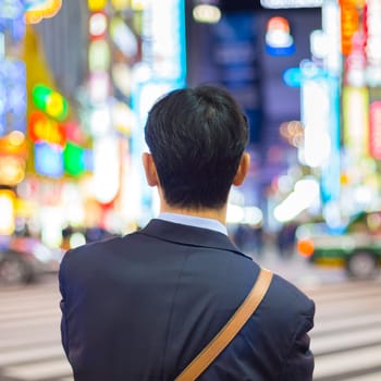 Solitary japanese corporative businessman in suit, after work, waiting on crossroad in Kabukicho, entertainment and red-light district in Shinjuku, Tokyo, Japan.