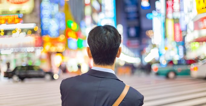 Solitary japanese corporative businessman in suit, after work, waiting on crossroad in Kabukicho, entertainment and red-light district in Shinjuku, Tokyo, Japan.