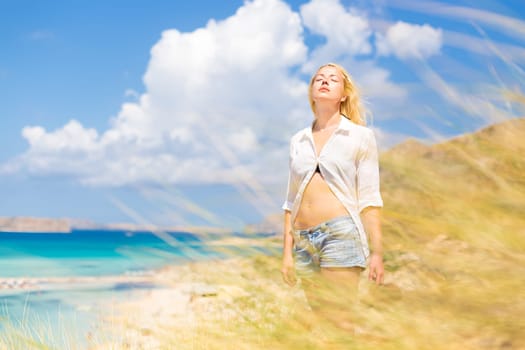 Relaxed woman enjoying freedom and life an a beautiful sandy beach.  Young lady feeling free, relaxed and happy. Concept of freedom, happiness, enjoyment and well being.  Enjoying Sun on Vacations.