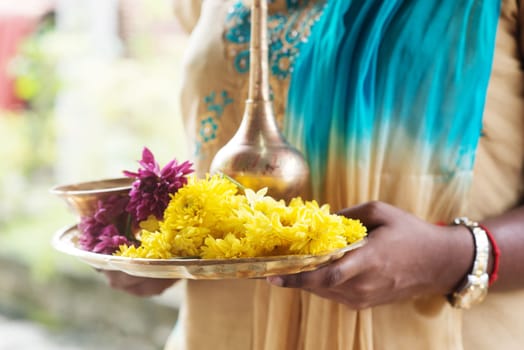 Indian girl with traditional plate of religious offerings and flowers for ear piercing ceremony.