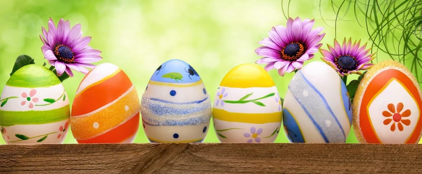 Colorful Easter eggs in a row,decorated with spring flowers and long grass,with bright green bokeh background,panorama format