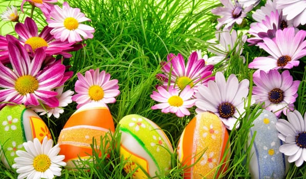 Spring flowers and happy colorful Easter eggs on fresh grass