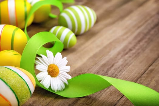 Neat Easter decoration with happy bright spring colors of green,yellow and white on a wooden surface,with a daisy flower,curved ribbon and painted eggs