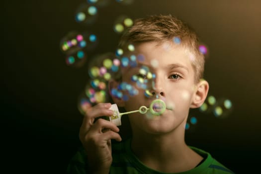 Young boy blowing iridescent soap bubbles at a party or celebration, close up with selective focus to his face in shadowy darkness