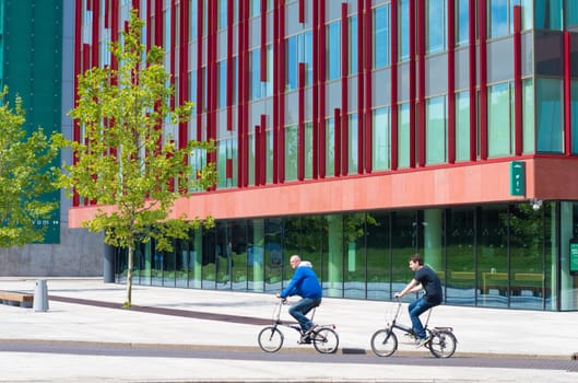bikers passing a modern office building in Almere, netherlands. It is the youngest and fastest growing city in the country, founded around 1975.