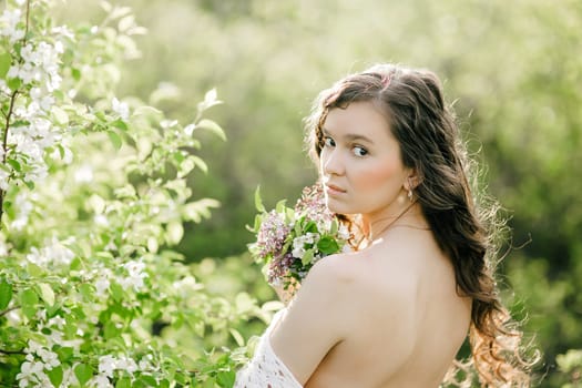 the young girl with a naked back costs in sun beams with a bouquet of wild flowers