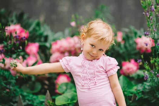 the little girl with white hair and blue eyes in a pink t-shirt poses against flowers