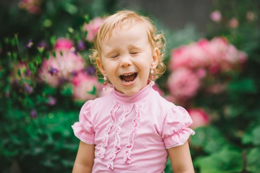 the little girl with white hair in a pink t-shirt poses with the narrowed eyes against flowers
