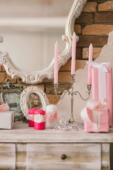 New Year's and Christmas interior in pink color with a dresser, a wall mirror, gifts, candles