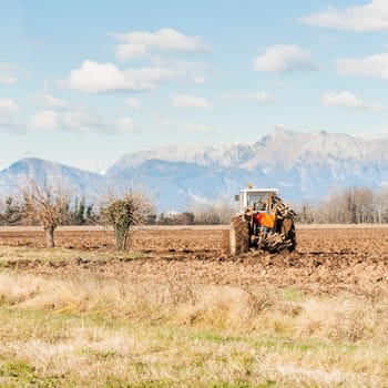 Agricultural landscape. With tractor plowing a field. The mountains in the background.