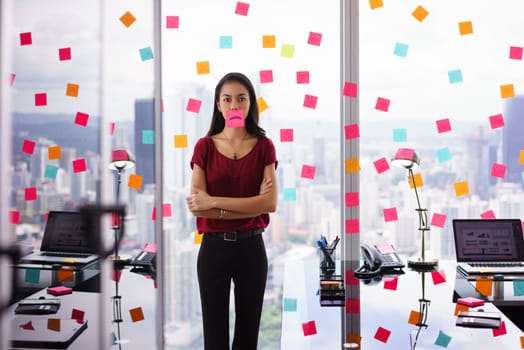 Mixed race woman working in modern office with reminders on skyscraper window. The girl feels stressed, holds a sticking note with sad emoticon on mouth.