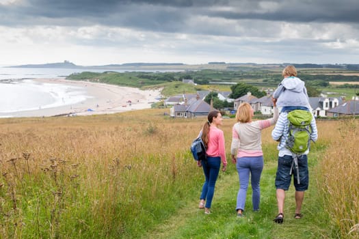 A fmaily of four are walking along the sand dunes. The little boy is getting carried on his fathers shoulders.