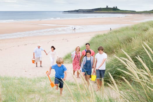 A family are walking up the sand dunes, leaving the beach. They are all smiling and talking with each other.