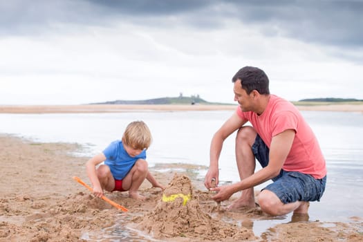 A little boy and his father are building sand castles on the beach.