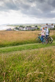 A couple are stood on the sand dunes with their bikes, they have stopped to enjoy the view.