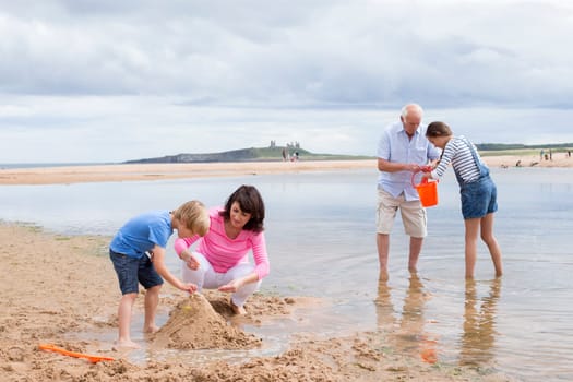 Grandparents and grandchildren are playing together on the beach. They all look happy playing with the sand and water.