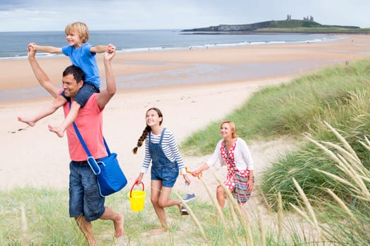 A family of four are leaving the beach together. The little boy i on his dads shoulder smiling.