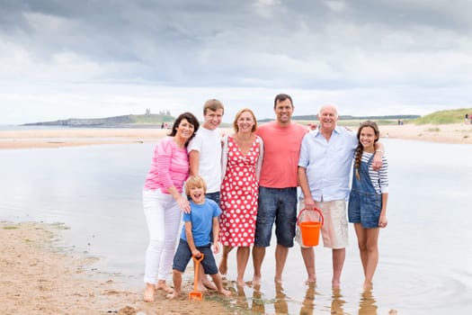 A family are on the beach with their feet in the water. They are all smiling, looking at the camera.