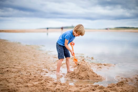 A little boy is at the beach building a sand castle.