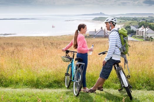 A father and daughter have stopped their bike ride to enjoy the view and chat. They both look happy and are smiling.