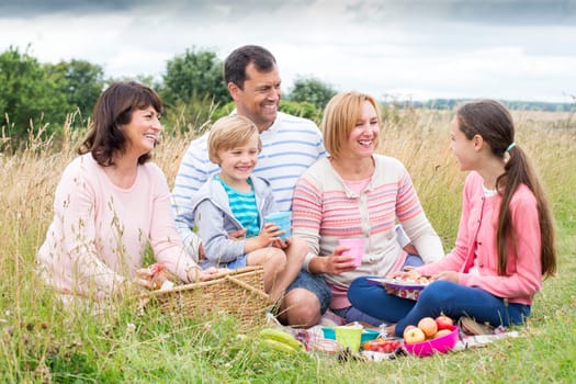A family are sat on the sand dunes having a picnic, They are all smiling, talking together