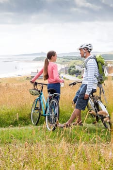 A father and daughter are on the sand dunes with their bikes. They have stopped to talk and enjoy the view.