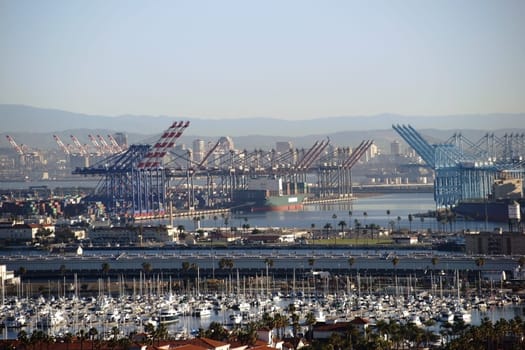 A residential area and sailboat port in front of the industrial port of Los Angeles with cranes,power poles and industrial buildings.