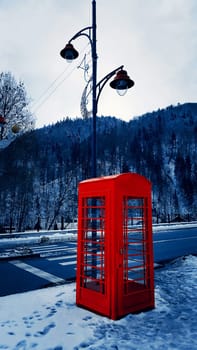 Classic red British telephone box on the snowy street in Sinaia, Carpathian Mountains, Romania.