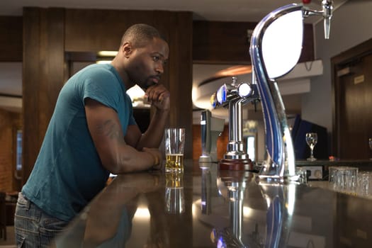 Young man standing at the bar looking deep in thought, with a pint in his hand.