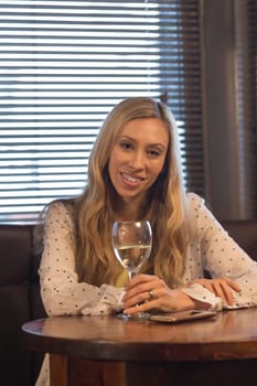 Attractive young woman sitting in a pub with a glass of wine and her smartphone. She is smiling at the camera.