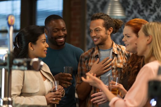 Group of friends drinking beer at a bar. They are all laughing and talking to eachother.