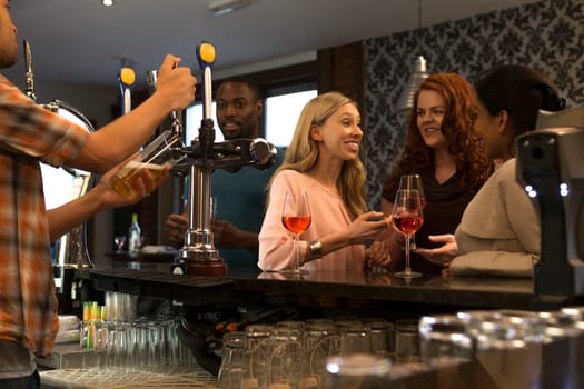 Group of people at a pub, enjoying drinks and talking. A bartender can be seen pouring a pint.