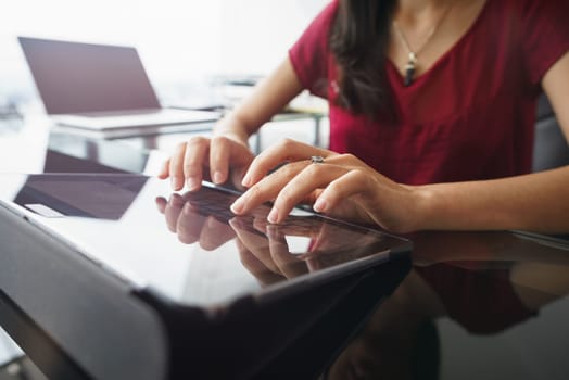 Closeup of hands of female computer technician sitting and typing on tablet computer with laptop in background