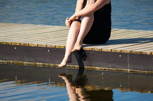 Young women sitting on the Jetty, with jer legs in the lake water