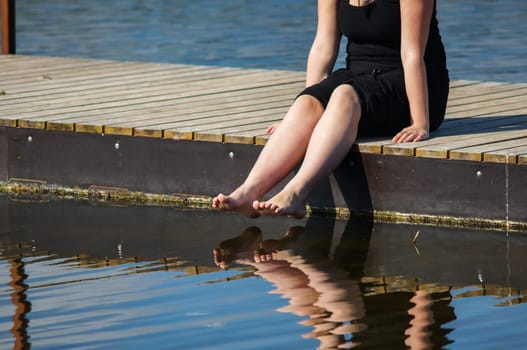 Young women sitting on the Jetty, with jer legs in the lake water
