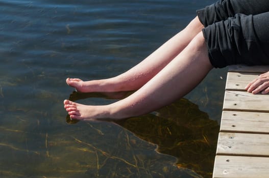 young lady dips her feet in the cool lake water on a sunny day
