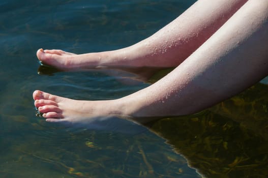 young lady dips her feet in the cool lake water on a sunny day