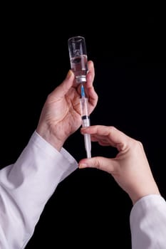 Filling of a syringe with medicine from vial. Medical person holding medical syringe and drug vial. Tip of needle shows. Isolated Black background.