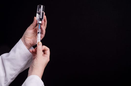 Filling of a syringe with medicine from vial. Medical person holding medical syringe and drug vial. Tip of needle shows. Isolated Black background.