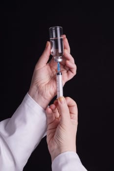 Filling of a syringe with medicine from vial. Medical person holding medical syringe and drug vial. Tip of needle shows. Isolated Black background.